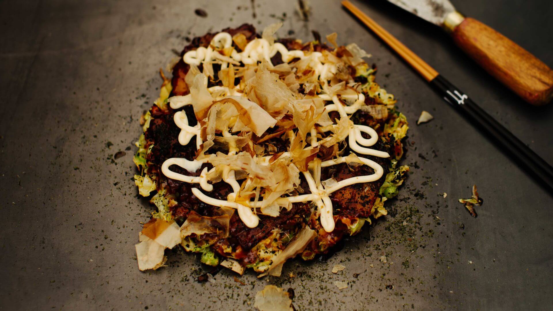 Okonomiyaki Osaka Style: Okonomiyaki im Osaka-Stil ist Japans Antwort auf den deftigen Pfannkuchen – herzhaft, sättigend, individuell. Hier wird alles miteinander vermengt: Teig, Weißkraut, Frühlingszwiebeln, dazu je nach Lust und Laune...