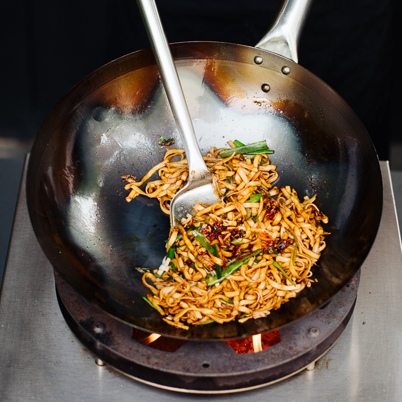 Wok de acero al carbono salteando fideos sobre llama alta